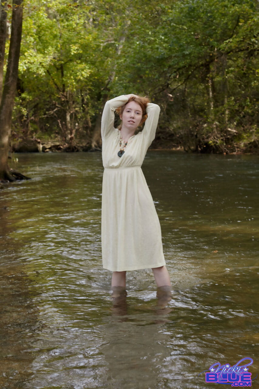 Natural redhead Nicki Blue shows some leg while wading into a shallow stream