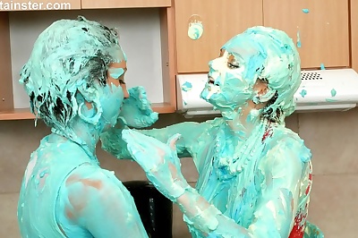 Clothed women cover each other in cake mix during a food fight in kitchen