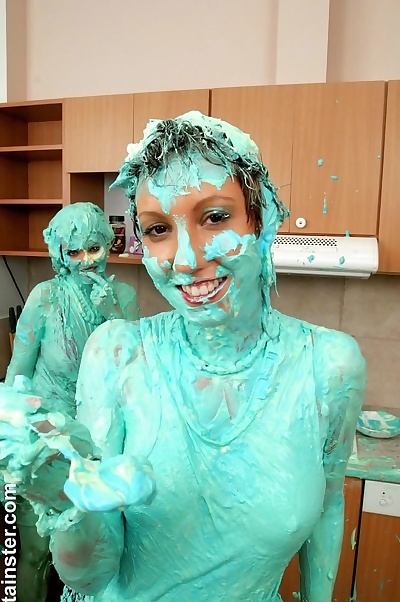 Clothed women cover each other in cake mix during a food fight in kitchen
